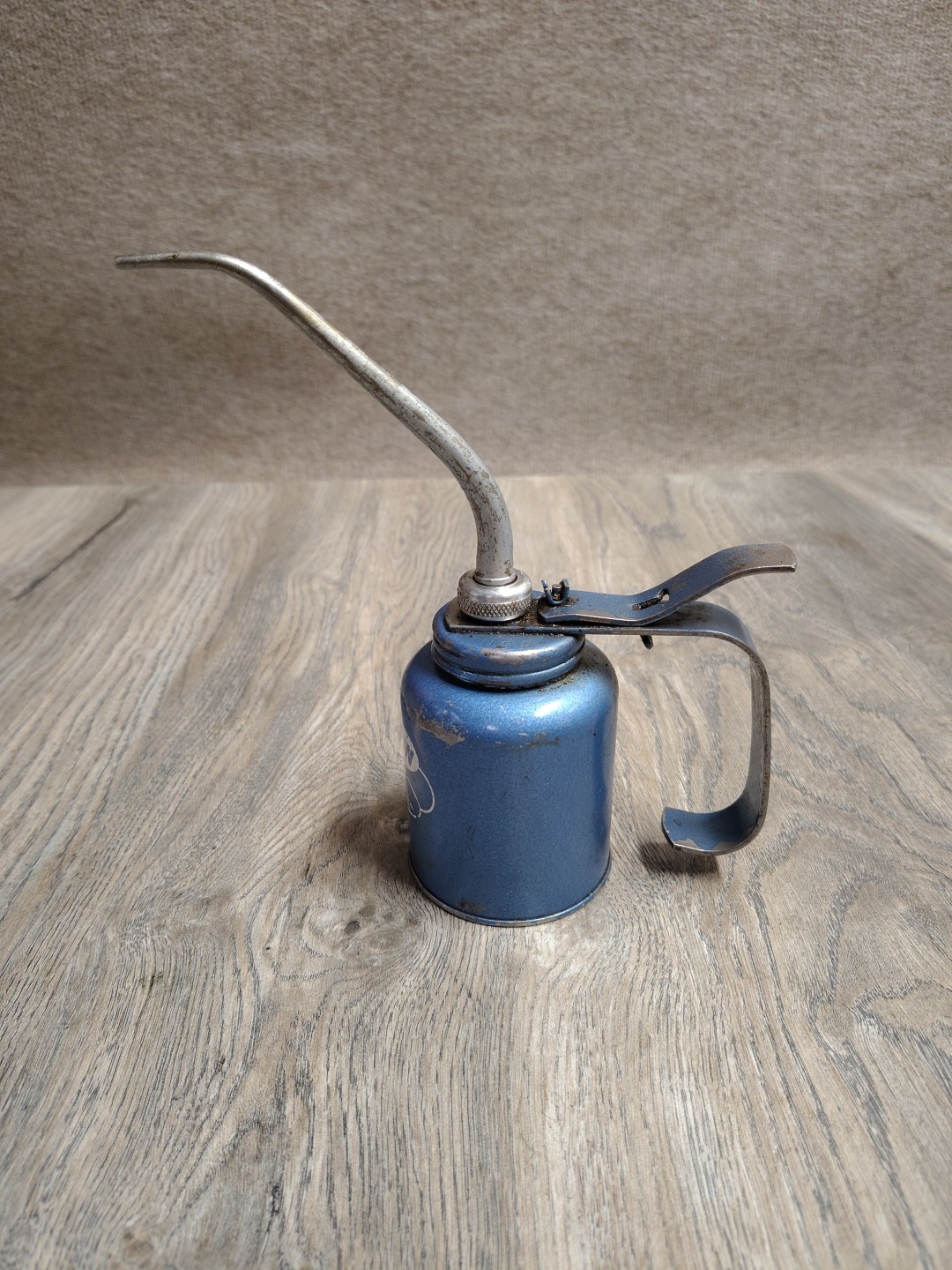 Vintage Plews metal pump oil can featuring a long rigid spout and classic thumb
