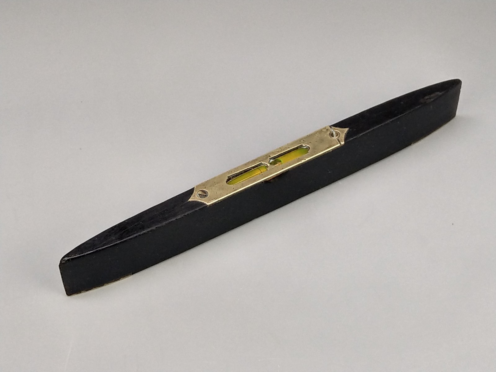 Antique spirit level made of ebony in a boat shape with brass shoes